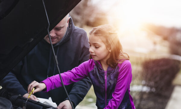 father and daughter checking oil in car