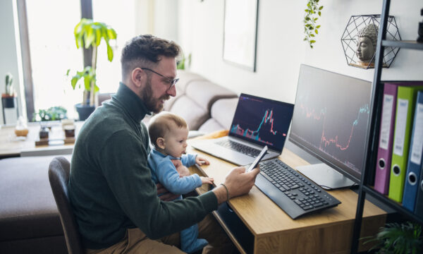 Person with baby looking at financial performance on computer in home office.